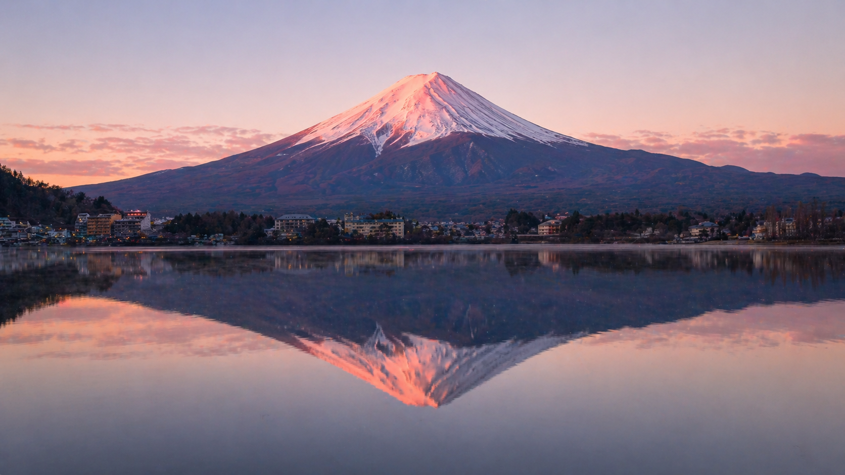 Mt. Fuji at sunrise from Lake Kawaguchiko with mirror reflection on still water and pink alpenglow